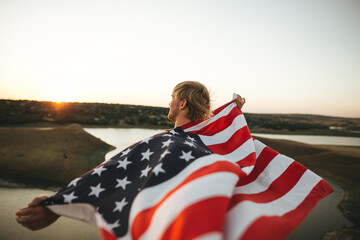 Young caucasian male energetically raised the US flag at sunset in mountain. 