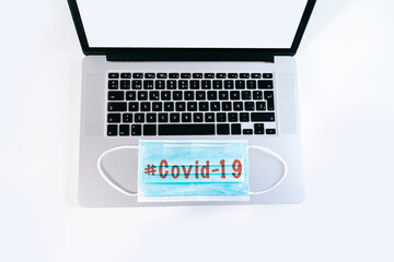 Laptop with a medical face mask on top with a message about covid-19. Concept of teleworking from home in times of coronavirus. Remote and online working.