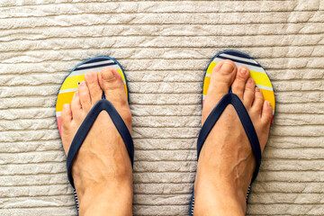 A pair of feet wearing flip-flops on the handwoven rug,top view