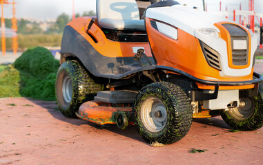 Tractor lawn mower close-up on the background of a heap of mown grass in the park. Lawn care concept.