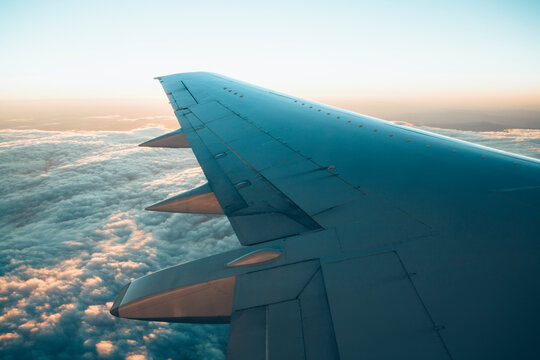Airplane wing through passenger window with dramatic sky at sunset