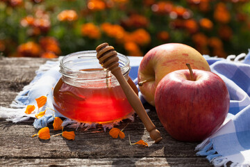 Honey in a glass jar and apples on an old wooden table in a flower garden, selective focus, blur. Religious holiday, postcard.