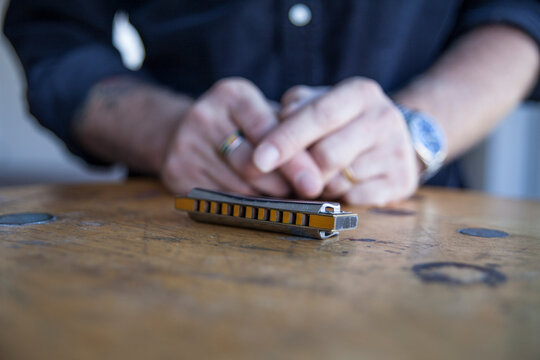 mans folded hands on table in front of harmonica