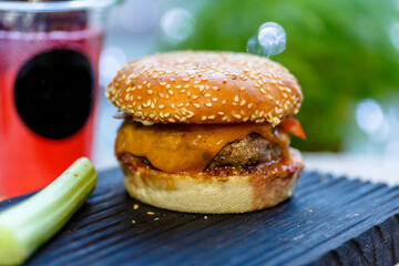 A Burger with beef and tomato cheese sits on a black wooden Board