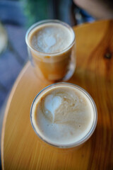 two cups of latte coffee drink with hearts made of foam in glassware standing on a yellow table