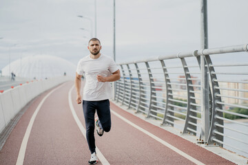 Fototapeta na wymiar athletic man dark-haired Caucasian appearance running on a treadmill white t-shirt, sports training in the city