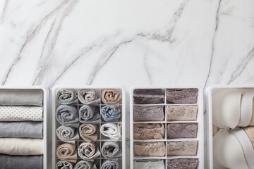Womans underwear, pajamas and socks neatly folded and placed in closet organizer drawer divider on white marble table.