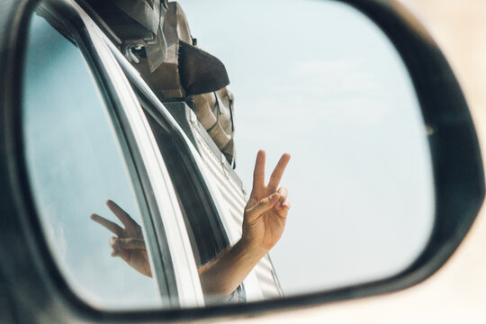 Hand making V sign out of the window of a car reflected on the car mirror