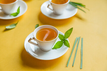 Herbal green tea with lemongrass in glass cup with fresh limes. Top view of three white cups of Lemon Grass Drink on a Yellow Background.