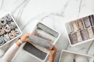 Woman hands neatly folding underwears and sorting in drawer organizers on white marble background.