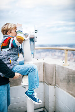 father holds his son up to look through coin operated binoculars