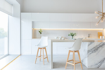 luxury interior design of modern trendy snow white kitchen in minimalistic style with island and two bar stools. huge windows to the floor and a glass rack for dishes