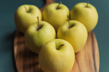 yellow golden delicious apples on green table, wooden cutting board 