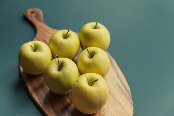 yellow golden delicious apples on green table, wooden cutting board 