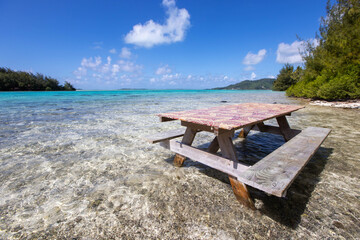 Picnic table in shallow, clear, tropical island ocean water on a private motu