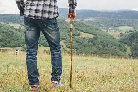 Young man wearing jeans, hicking with his walking stick in the mountains