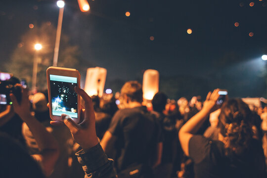 Festival time - People taking photos on phone of fire lanterns flying in the night sky