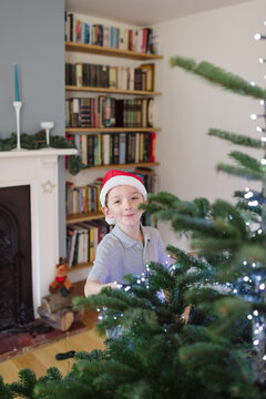 Boy in Christmas hat peeps around his Christmas tree