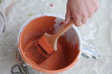 Dipping Paintbrush in Pail of a Orange Paint