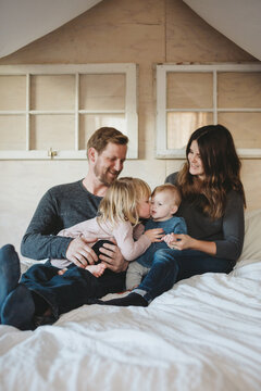 Trendy young family hugging together inside on white bed in winter - candid