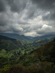 Fototapeta na wymiar Moody vertical landscape of mountains and green valley and forest with trees with a beautiful dark sky with clouds in Salento, Colombia