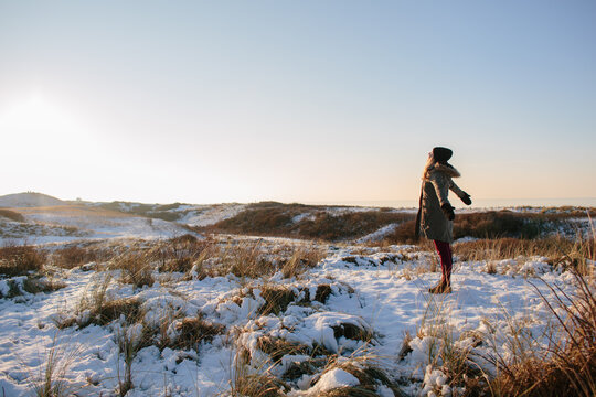 A woman standing in a snowy field looking at the sun.