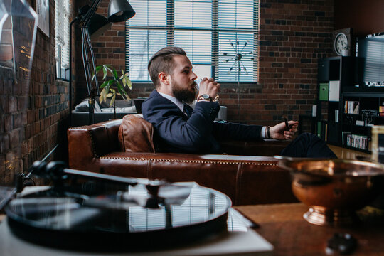 Young man drinks while sitting by record player
