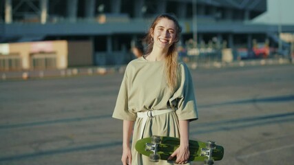 Smiling young woman look at camera happyholding skateboard outdoors trendy urban outside hipster board street style slow motion