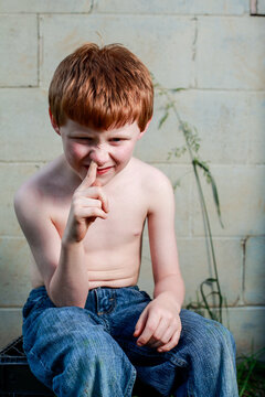Young redheaded boy picking nose with shirt off