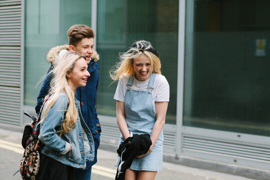 Three teenagers laughing together in the street.
