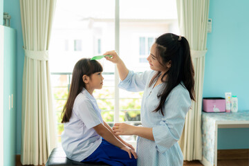 Asian Mother is combing her daughter's hair on the morning before going to school in living room at home. The morning school routine for day in the life getting ready for school