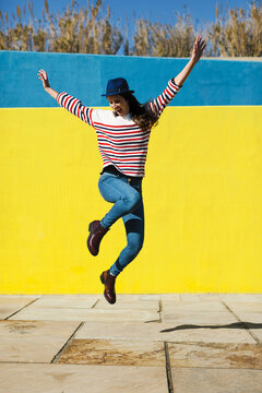 Happy young woman jumping in front of yellow background.