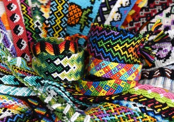 Tied woven DIY friendship bracelets on background of many multi-colored friendship bracelets handmade of embroidery bright thread with knots.