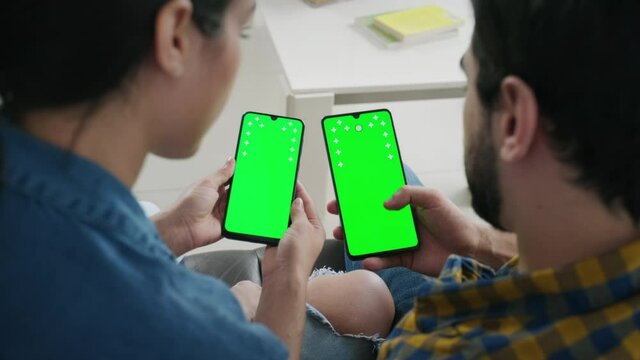 Young people using cell phones with green screen for internet and social media. Man and woman holding smartphones for web site. Boyfriend and girlfriend watching movie and photos on mobile telephones