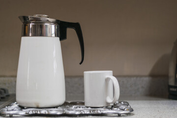 Old coffee maker beside a cup of coffee in a kitchen