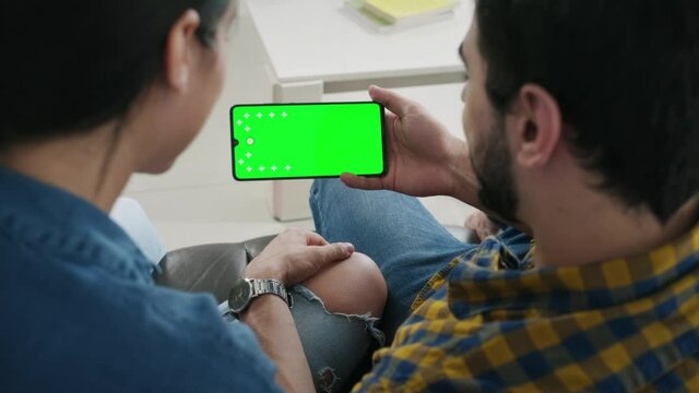 Young couple using cell phone with green screen for internet and social media. Man and woman holding smartphone with green monitor for website. Friends watching movie and pictures on mobile telephone