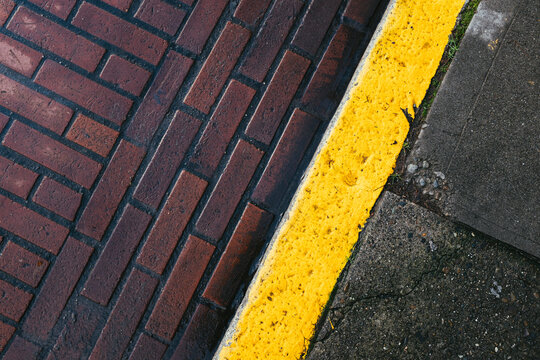 Painted yellow curb along brick sidewalk and street