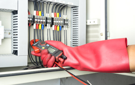 Electrician technician using digital Camp amp meter to check electric current in a factory  electrical installation with  hands protected by electric hand gloves