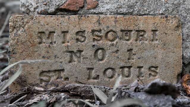 Close up of a vintage concrete brick cornerstone engraved with St Louis Missouri. Soft blurred background and overgrown grass and vegetation. 