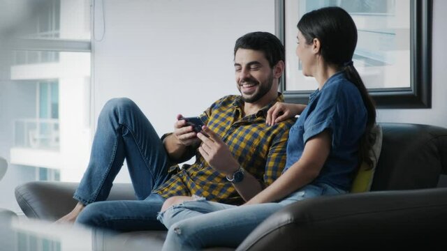 Young couple smiling, using cell phone for internet and social media. Happy man and woman holding smartphone for web site. Friends watching funny film and pictures on mobile telephone