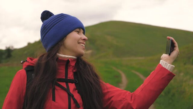 free Young girl tourist blogger records selfie videos at foot of mountains using a smartphone with beautiful landscape in background. Healthy cheerful woman travels and photography nature by phone.