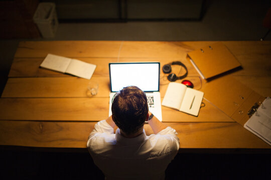 Young man working overtime in a dark office behind his laptop