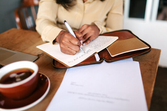 A woman sitting a wooden coffee table and writing notes in her leather journal
