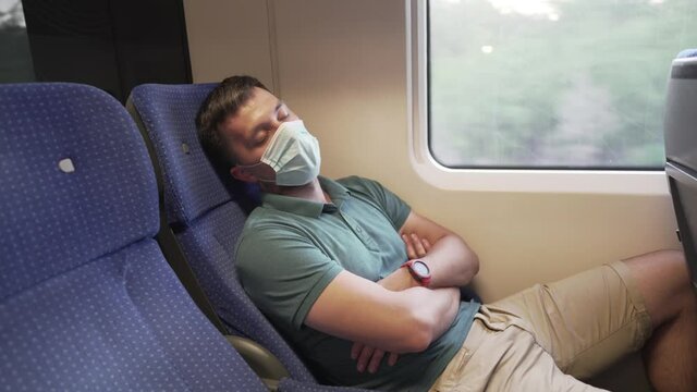Tired sleeping train commuter wearing PPE face mask for safety. Concept travel during pandemic. Protective medical mask during the trip. Medical respiratory bandage face in transport