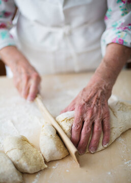 Woman cutting pieces out of fresh homemade dough with wooden cutter