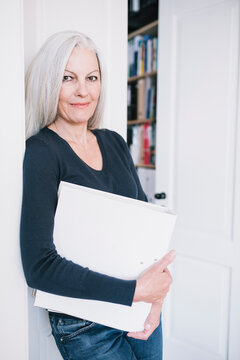 Senior woman standing a door case, holding a folder.