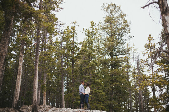 Engaged couple standing and hugging, laughing in forest in Banff National Park