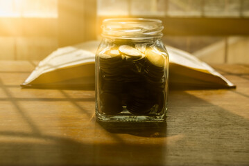 A glass jar to put coins on a wooden table and a notebook for saving ideas.