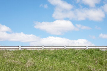Road Guardrail and Green Grass under a Blue Sky with Cumulus Clouds