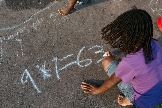 African American girl writing a multiplication on the ground with chalk